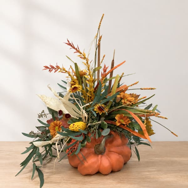 Fall floral arrangement in a pumpkin container with orange and yellow blooms