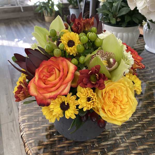 Mixed bouquet with roses, orchids, and yellow daisies in a dark vase