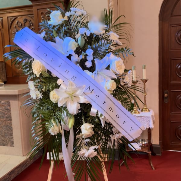 White funeral standing spray with lilies, roses, and a memorial sash
