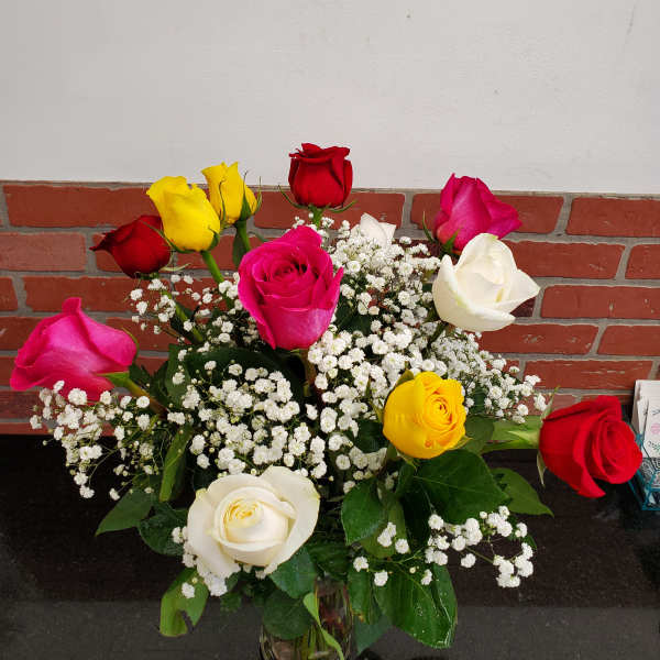 Mixed red, pink, yellow, and white roses with baby's breath in a clear glass vase on a dark countertop