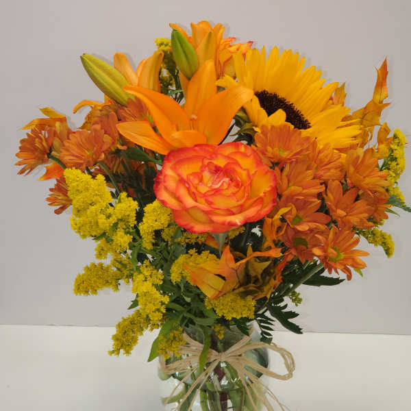 Orange and yellow bouquet in a glass vase with a raffia bow