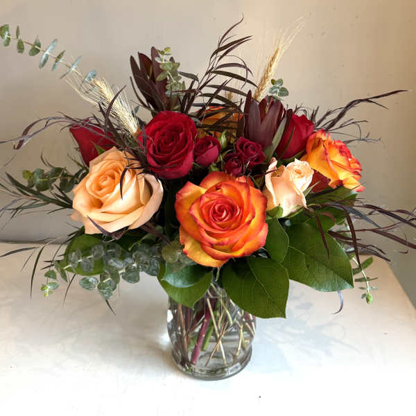 Mixed roses arranged in a clear glass vase with dark foliage.