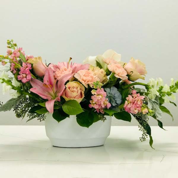 Pink and peach floral arrangement in a white container