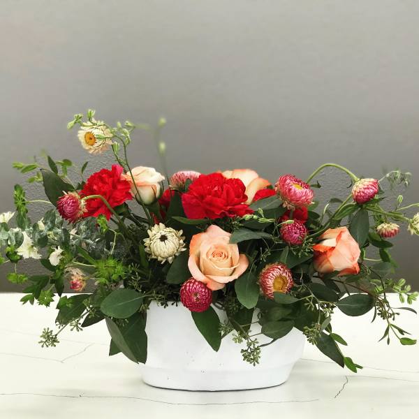 Mixed bouquet of roses and red carnations in a white container