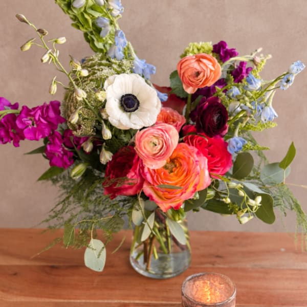 Mixed bouquet of colorful flowers in a clear glass vase with a candle nearby