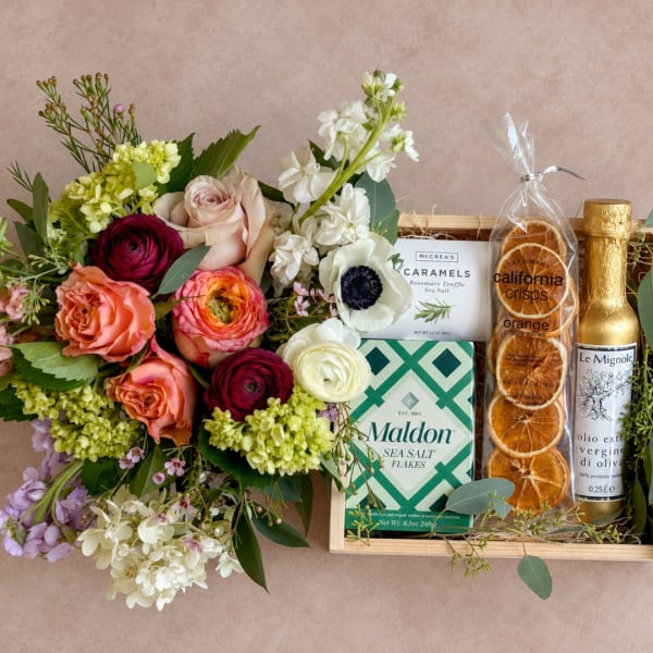 Mixed flower bouquet beside a gift tray with snacks and olive oil