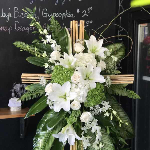 White lilies and roses arranged on a wooden cross with green foliage