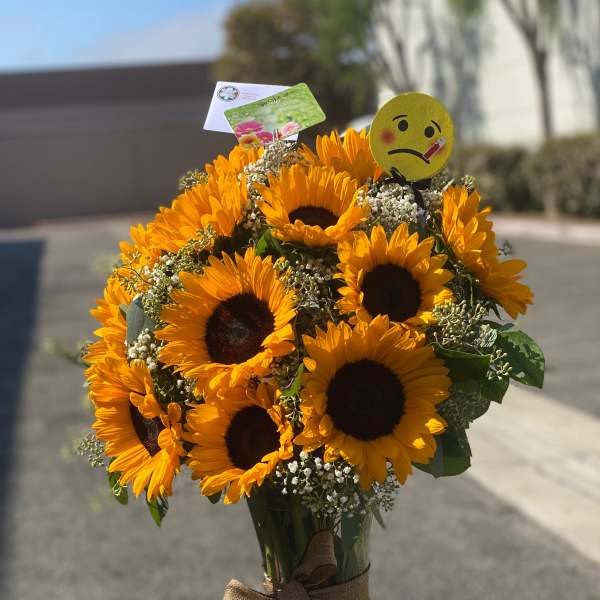Bouquet of sunflowers in a glass vase with a ribbon and emoji pick
