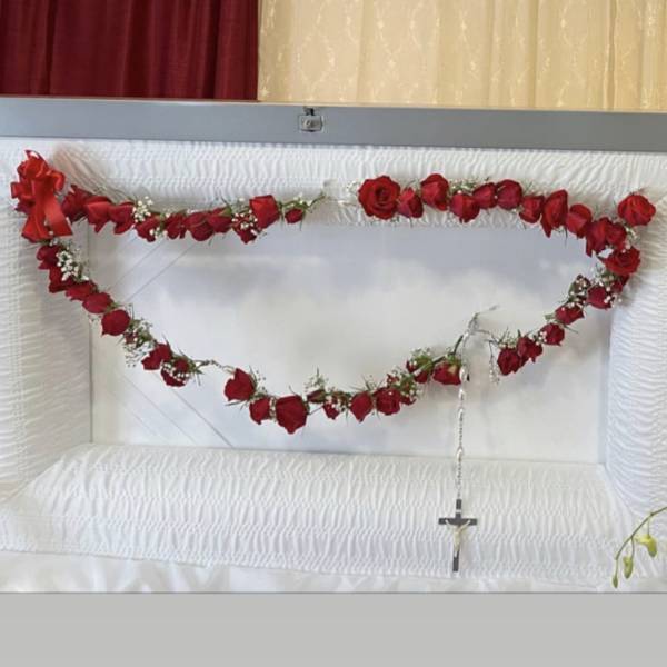 Red rose garland draped across a white casket with a cross pendant