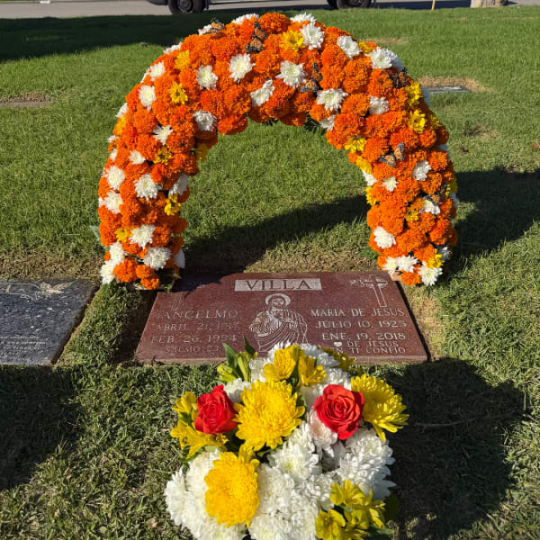 Orange, white, and yellow floral arch over a grave marker with a bouquet in front