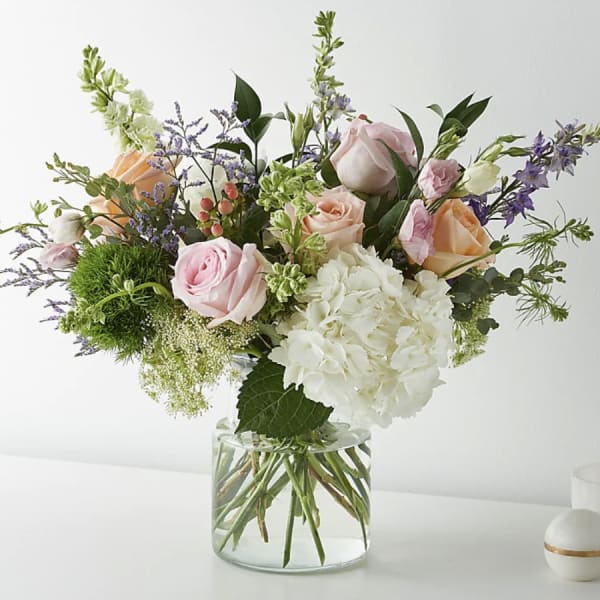 Mixed bouquet of pink and peach roses with white hydrangea in a glass vase