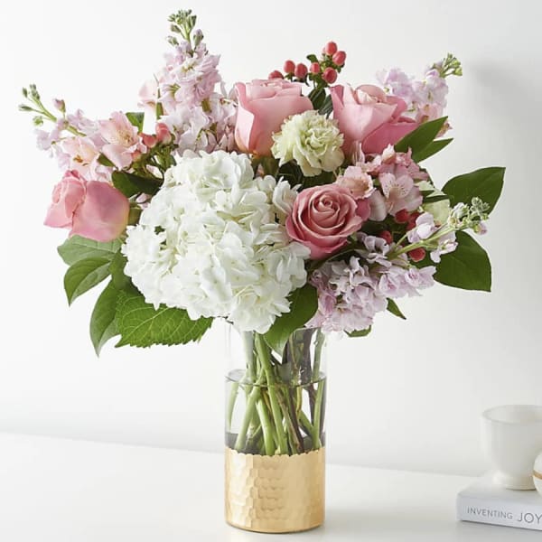Pink and white flower bouquet in a clear vase with a gold base