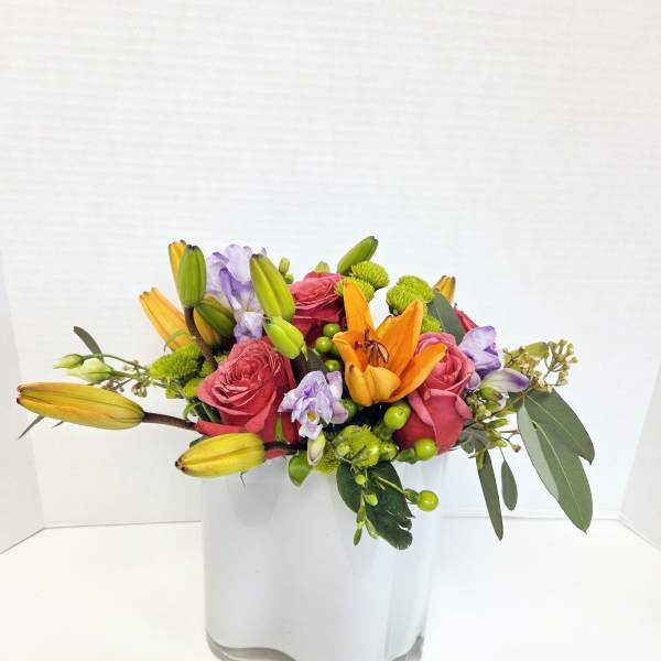 Mixed bouquet of pink roses, orange lilies, and purple flowers in a white vase