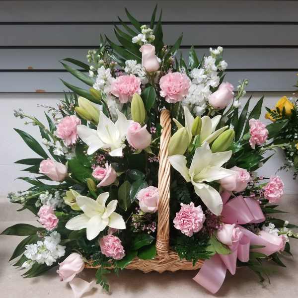 Basket arrangement of pink roses, white lilies, and carnations with a pink ribbon