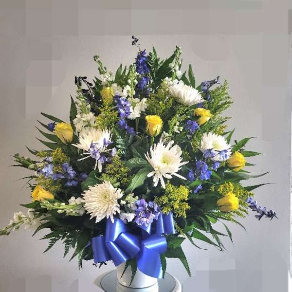 Large bouquet of white and yellow flowers with a blue ribbon in a white vase