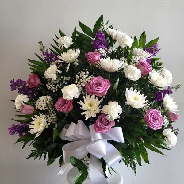Bouquet of pink roses, white daisies, and purple flowers with a white ribbon