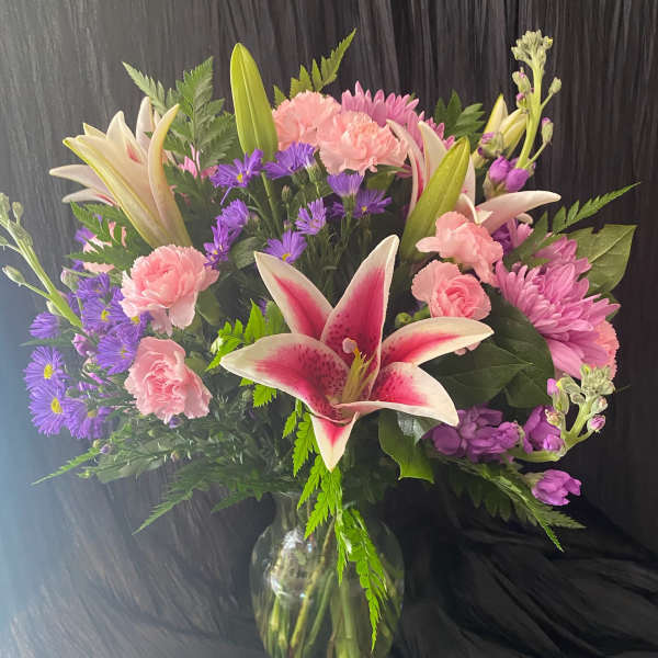 Bouquet of pink lilies, carnations, and purple daisies in a glass vase