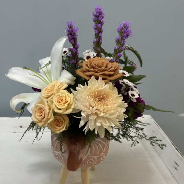 Mixed flower arrangement in a patterned ceramic mug on a small stand