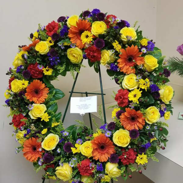 Large circular floral wreath on a stand with yellow, orange, red, and purple flowers