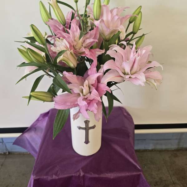 Pink lilies arranged in a white vase with a cross emblem