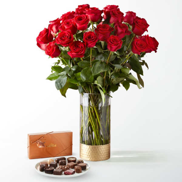 Red roses in a glass vase with a box of chocolates and a plate of candies