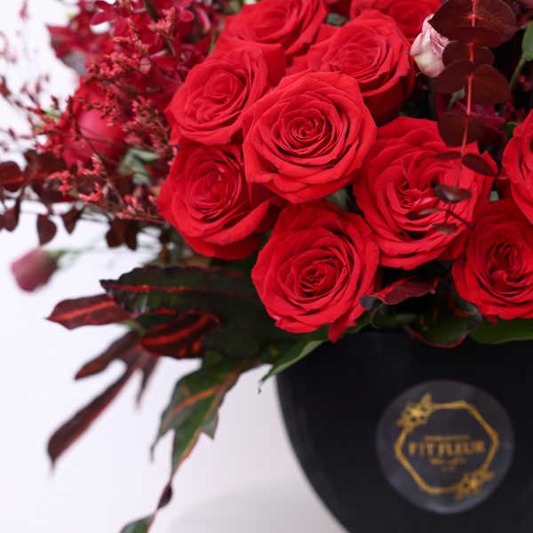 Red roses arranged in a black vase with dark foliage