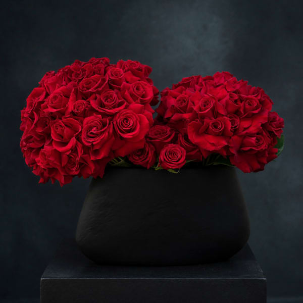 Two dense red rose bouquets in a black vase on a pedestal