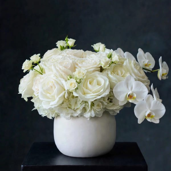 White rose arrangement in a round white vase with orchid blooms