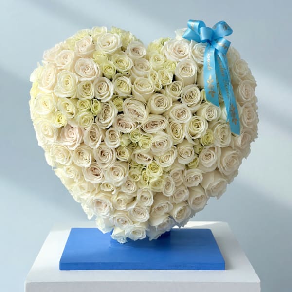 Heart-shaped bouquet of white roses with a blue ribbon on a pedestal