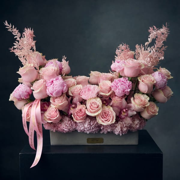 Pink roses and peonies arranged in a rectangular box with a ribbon