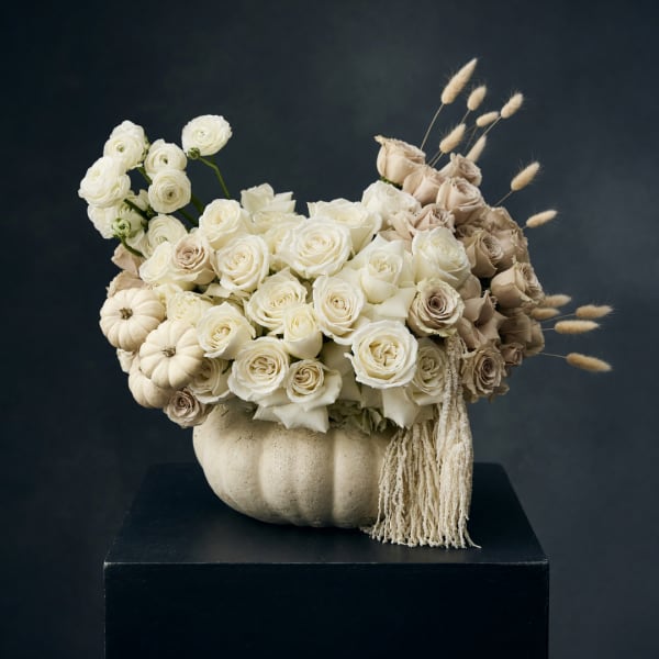 Cream rose arrangement in a white pumpkin vase with dried grasses