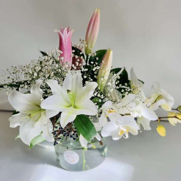 White lilies and pink buds arranged in a clear glass vase