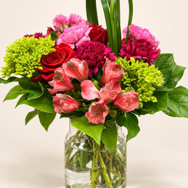 Mixed bouquet of pink, red, and lime flowers in a clear glass vase