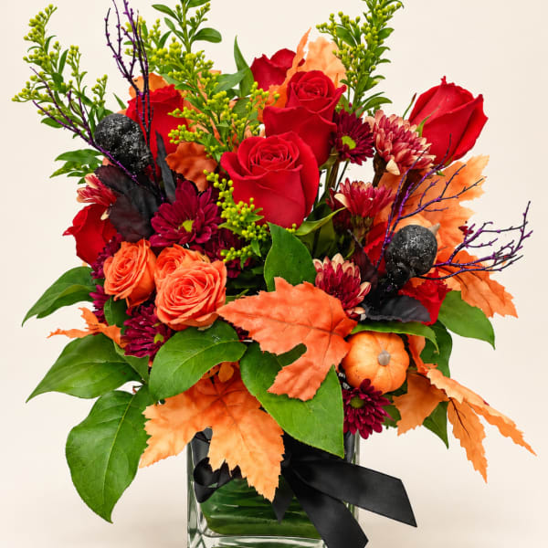 Autumn bouquet of red and orange flowers in a glass vase with black ribbon