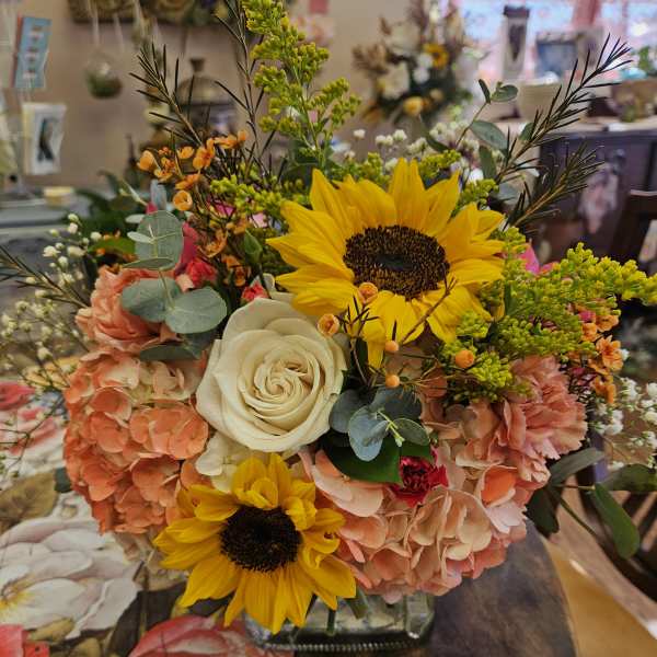 Bouquet with sunflowers, white roses, and peach hydrangeas in a glass vase