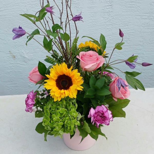 Pink roses and a sunflower in a pale pink vase with purple blooms