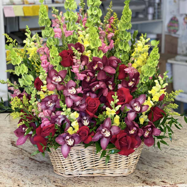 Basket arrangement of red roses, purple orchids, and green snapdragons