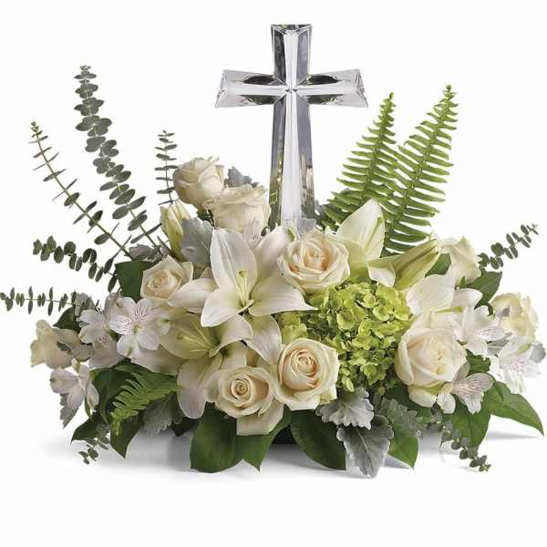 Low arrangement of white lilies and roses with green hydrangea and a clear crystal cross in the center