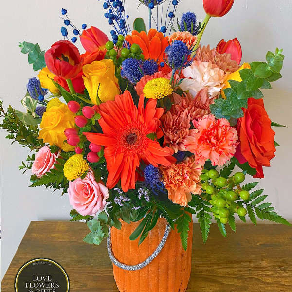 Bright mixed bouquet of orange, yellow, red, and pink flowers in an orange pot