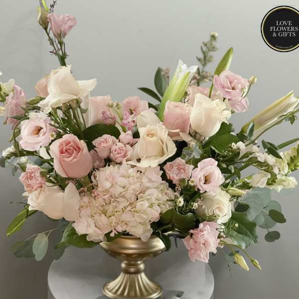 Low arrangement of pink and white roses, lilies, lisianthus and hydrangeas in a gold pedestal bowl