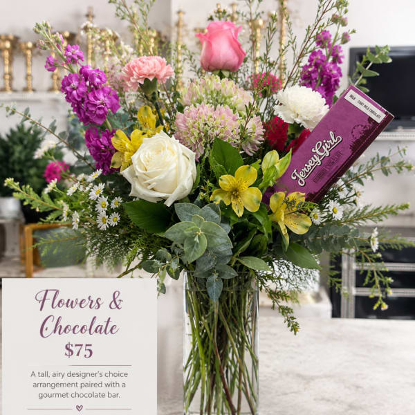 Tall mixed bouquet in a glass vase with a chocolate bar tucked in.