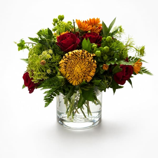 Bouquet of red roses and orange flowers in a clear glass vase