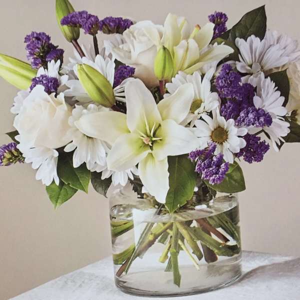 White lilies, daisies, and purple filler flowers in a clear glass vase