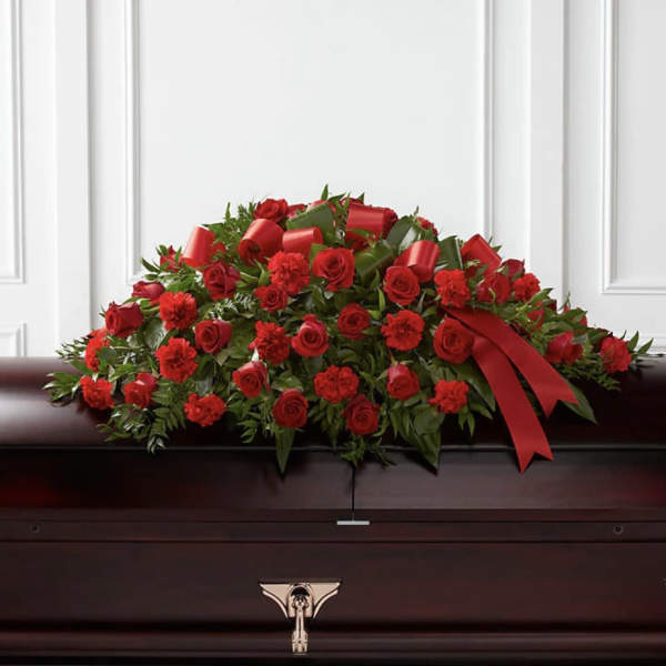 Red rose and carnation casket spray with ribbon on a dark coffin