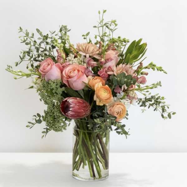 Mixed bouquet of pink and peach flowers in a clear glass vase