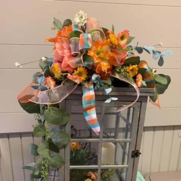 Colorful floral arrangement on a gray lantern with ribbons and trailing greenery