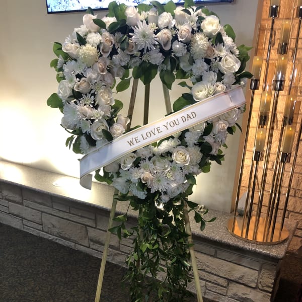 White floral standing wreath on an easel with a memorial ribbon