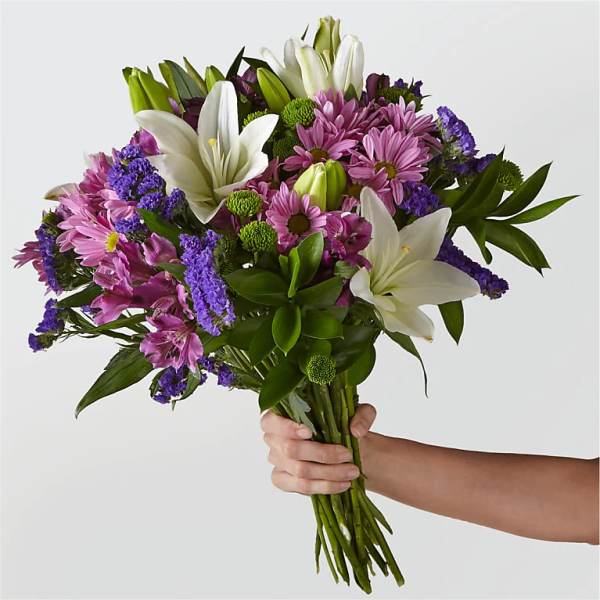 Handheld bouquet of white lilies, pink daisies, and purple filler flowers