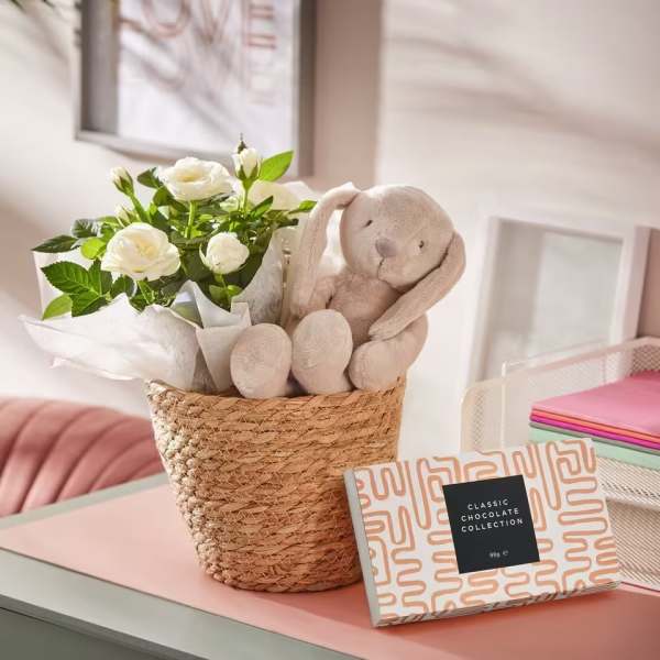 White rose bouquet in a woven basket with a plush bunny and chocolate box