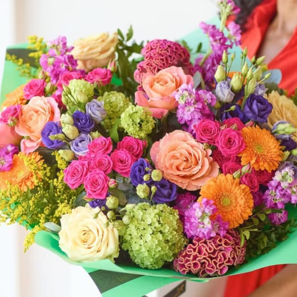 Colorful bouquet of roses, gerbera daisies, and mixed blooms wrapped in green paper
